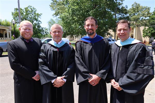 Four men including Donte Little, Andy Keith, Brodie Croyle, and Dr. Gilliam pose together and smile at the camera. The each wear their black ceremonial robes. 